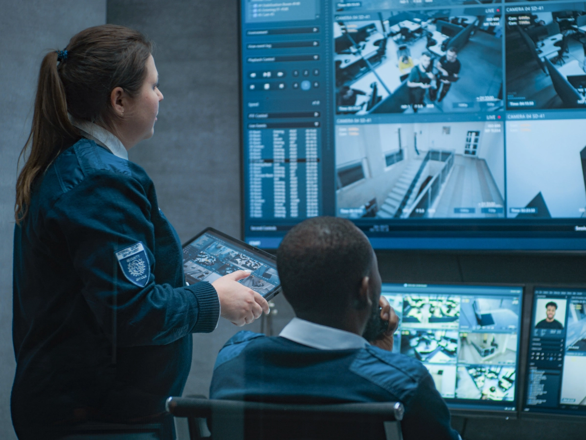 Security personnel review surveillance video on multiple digital monitors.